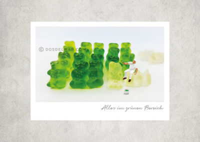 Postkarte Kleine Freiheit, Miniaturwelten, Miniaturfotografie. Miniaturfigur malt weiße Gummibärchen mit grüner Farbe an.